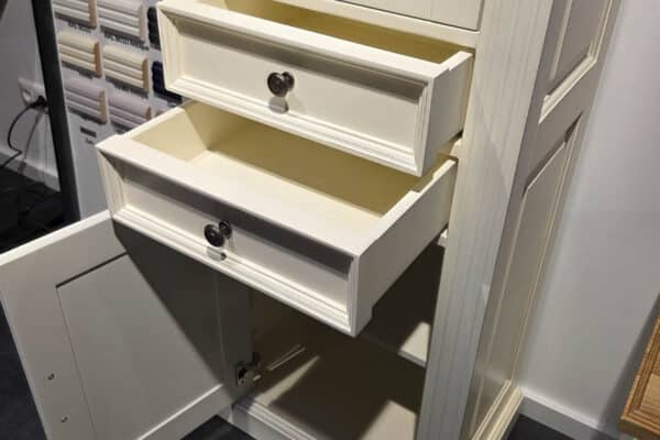 Offener weißer Holzschrank mit Tassen und drei Schubladen